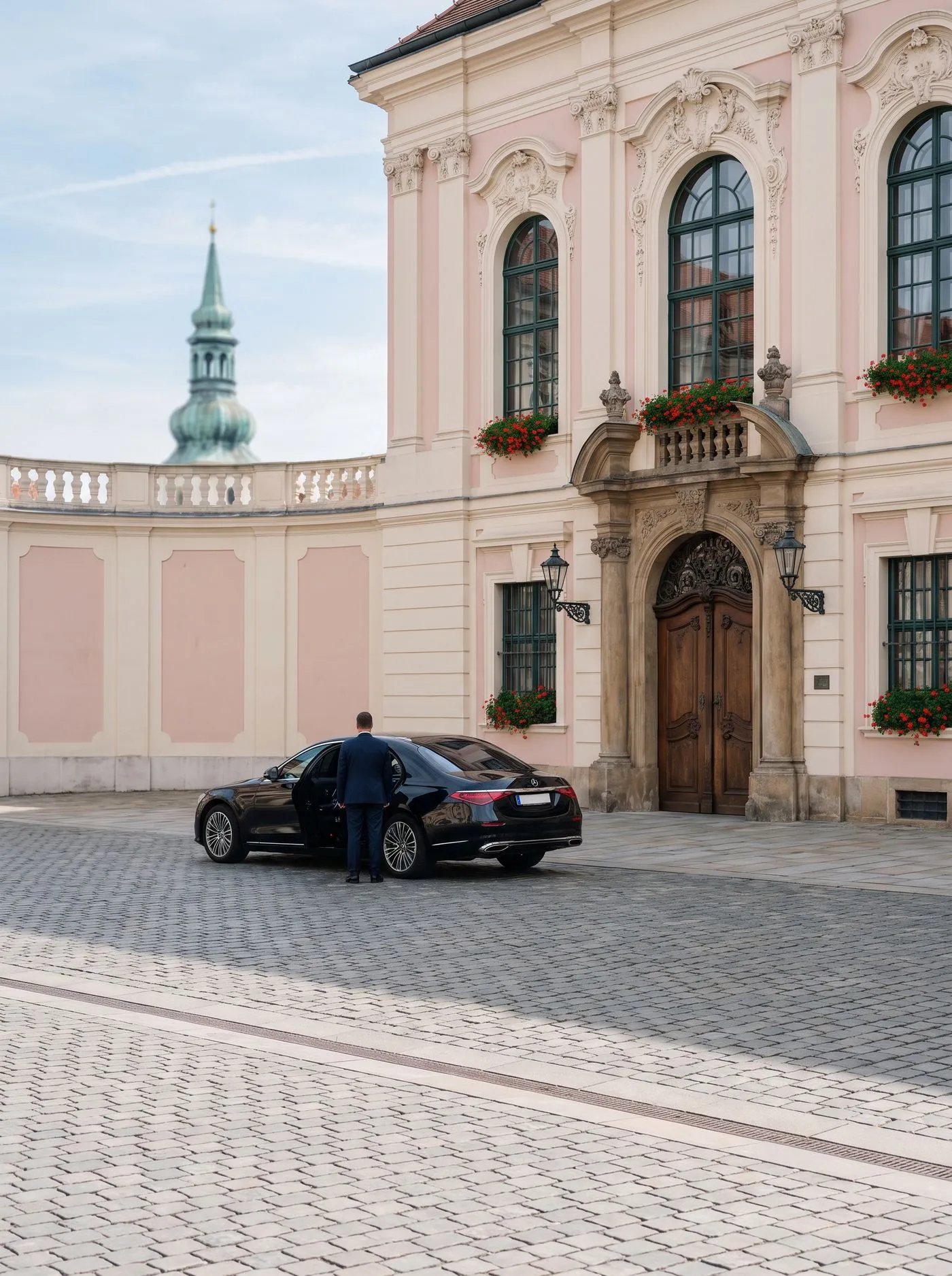 Limousine vor einem rosafarbenen Palais mit Kirchturm im Hintergrund