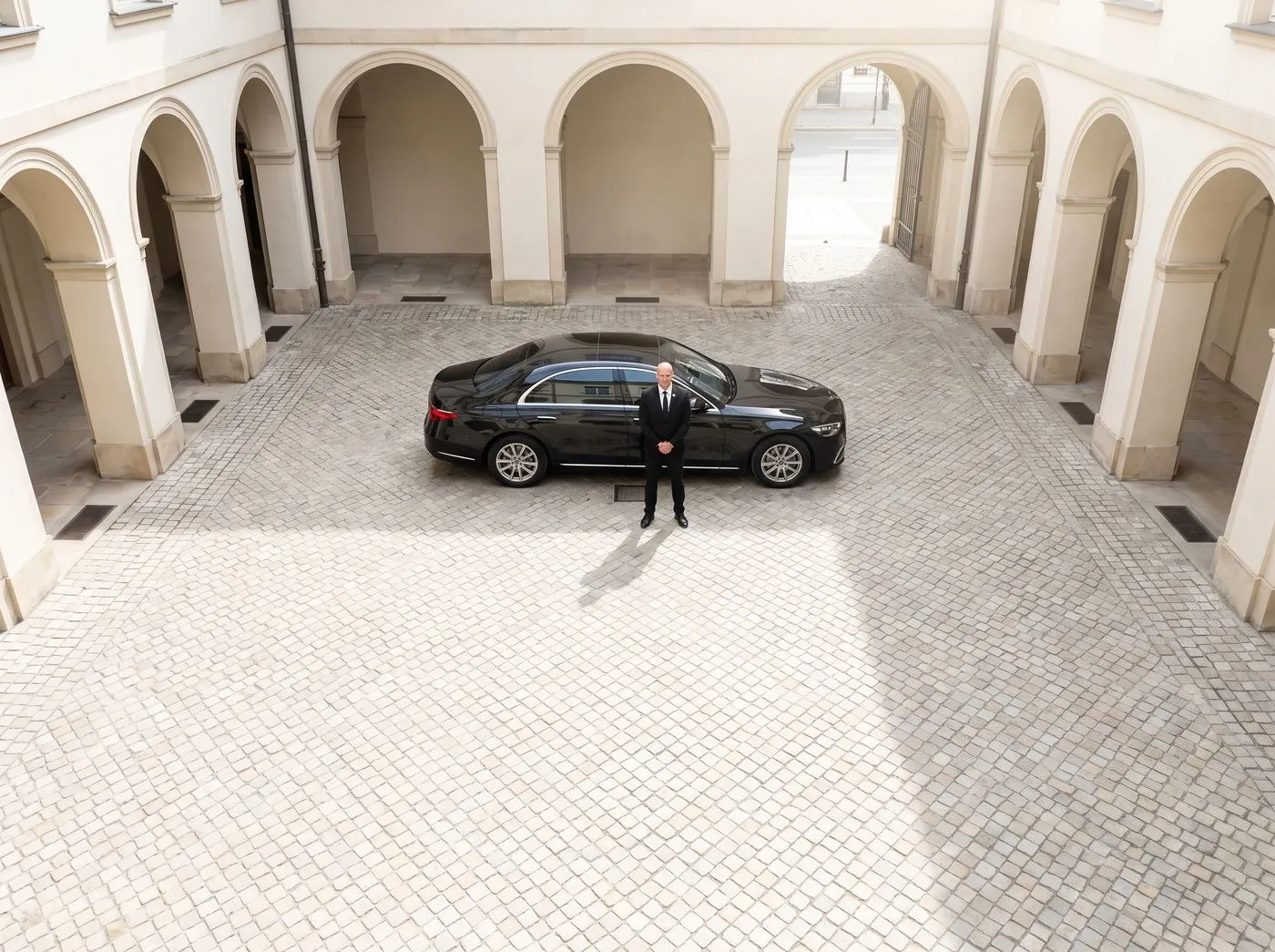 Schwarze Limousine in einem hellen Innenhof, der Chauffeur wartet daneben